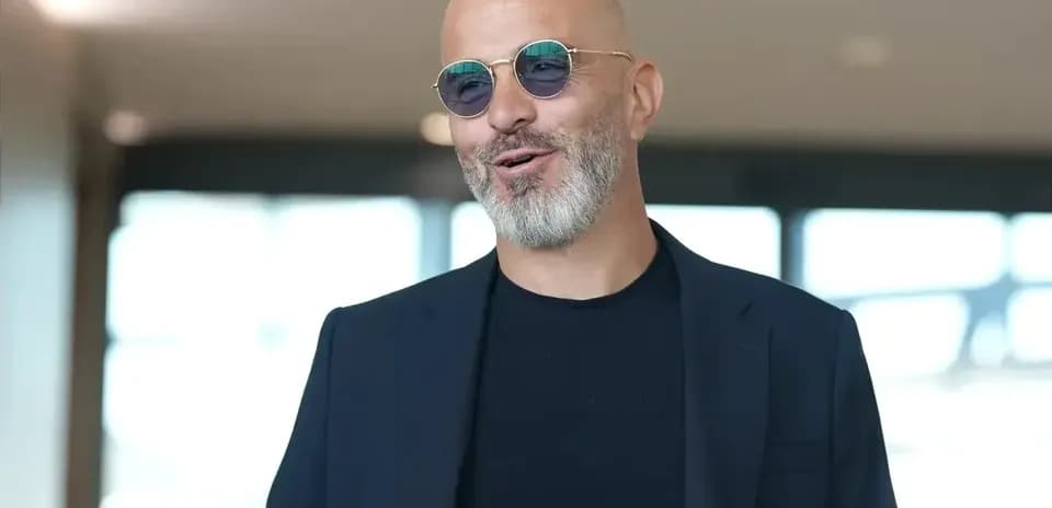 Person wearing sunglasses and a dark blazer indoors