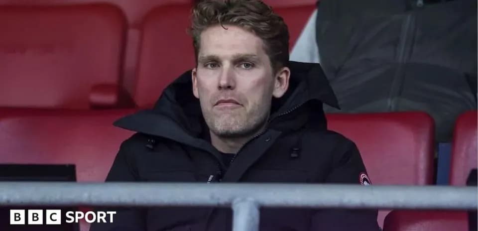 Man sitting in empty stadium seats, wearing black coat
