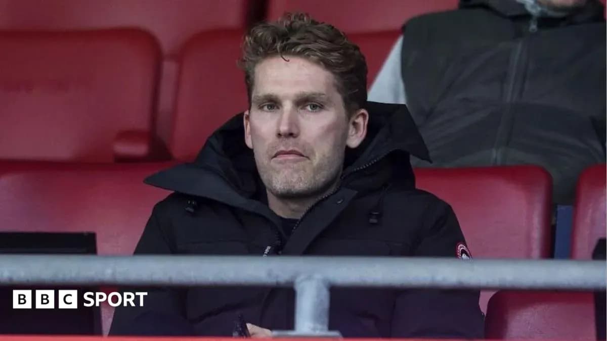 Man sitting in empty stadium seats, wearing black coat