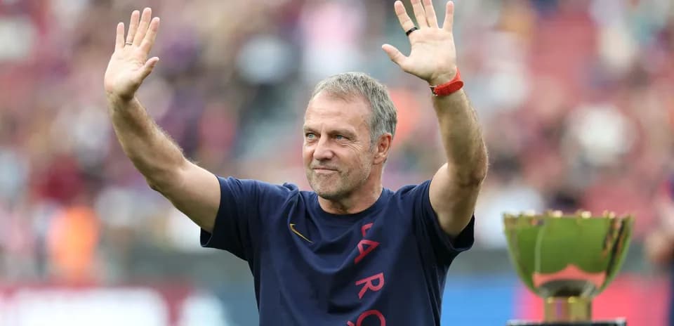 Coach waving to fans beside a trophy