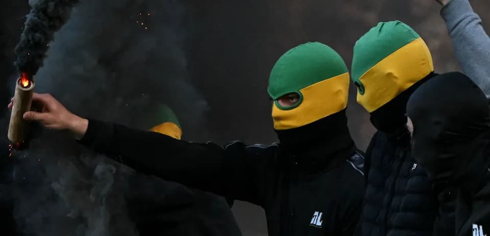 Masked individuals holding a flare amidst smoke