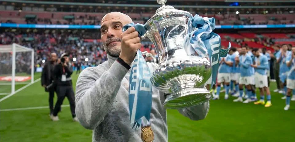 Manager holding trophy with team celebrating behind