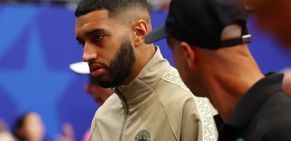 Player in warm-up jacket conversing with staff member