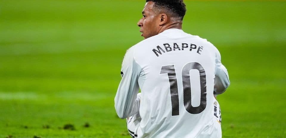 Player sitting on field wearing jersey with 'Mbappé' 10