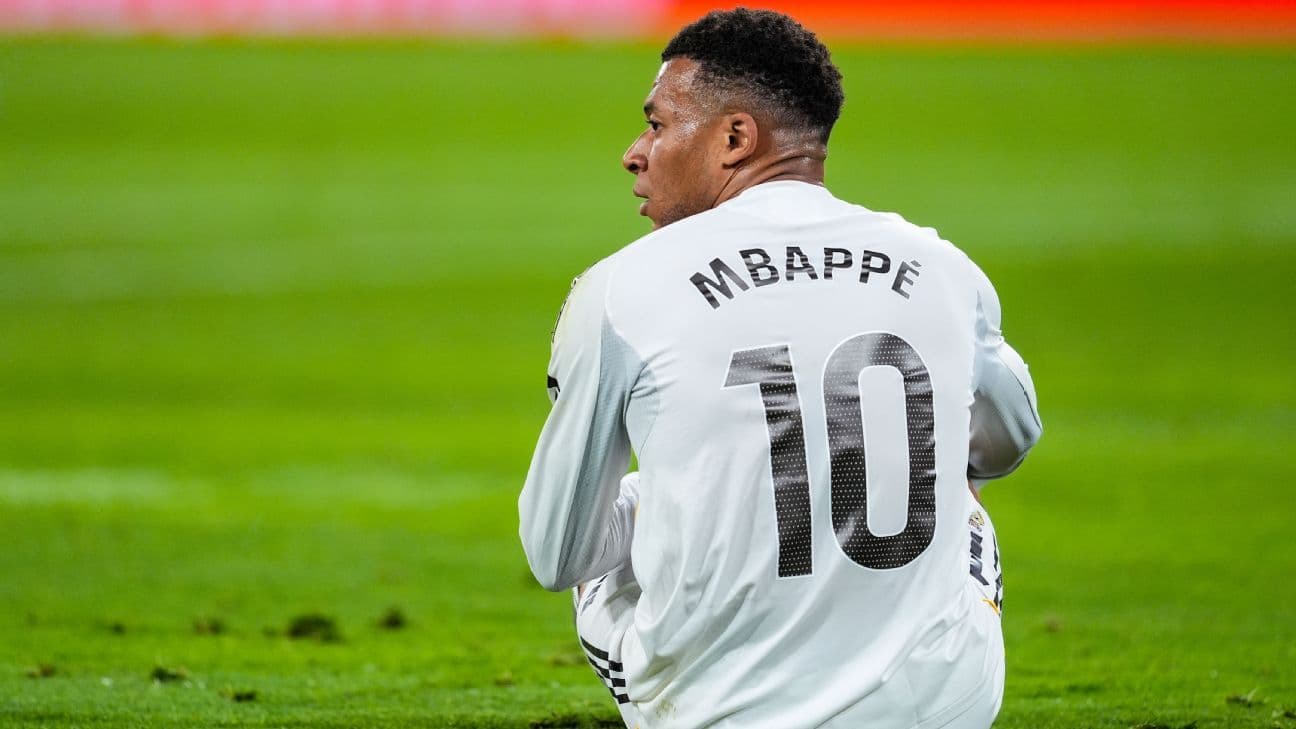 Player sitting on field wearing jersey with 'Mbappé' 10