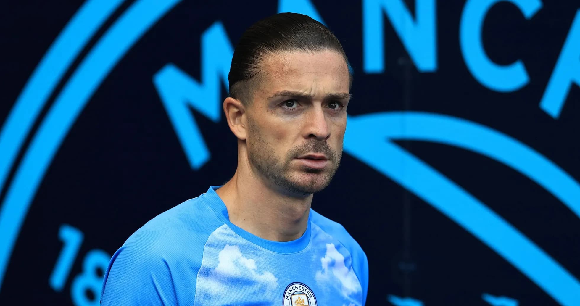 Player in blue kit standing before Manchester City backdrop