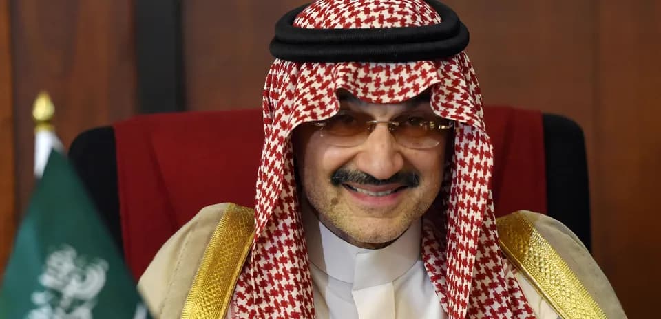 Man in traditional attire seated with Saudi flag