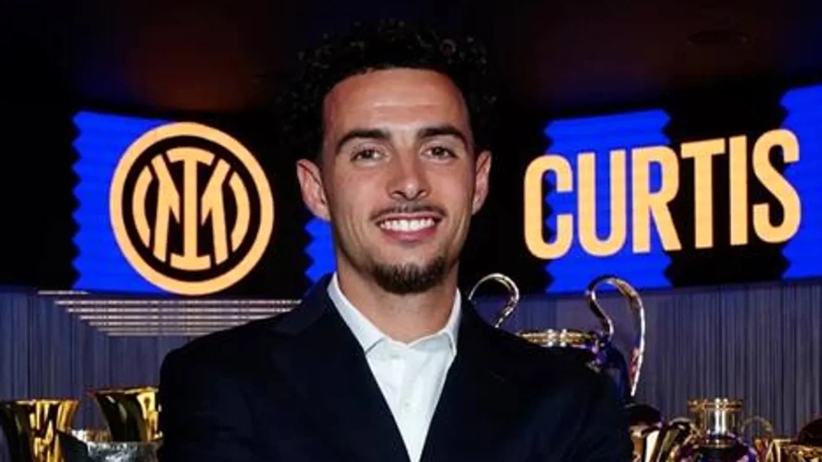 Player smiling at press event with trophies behind