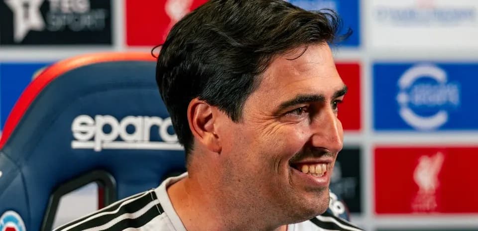 Coach smiling during press conference in front of logos