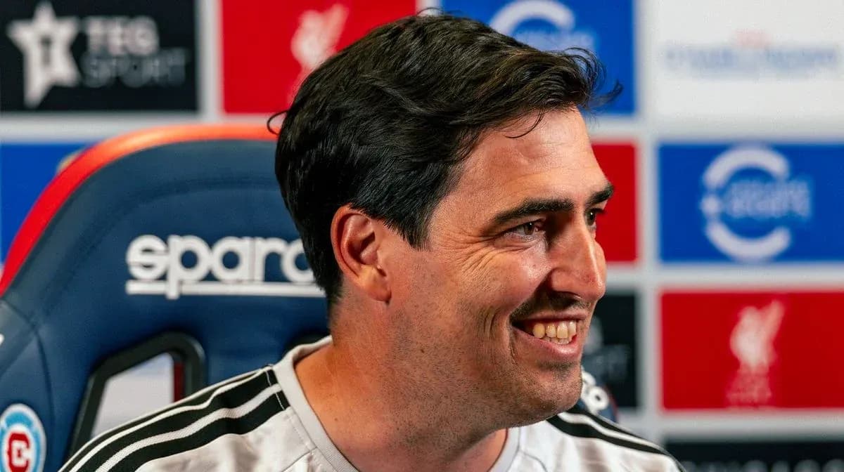 Coach smiling during press conference in front of logos