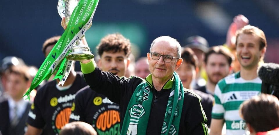Manager holding trophy with team celebrating behind
