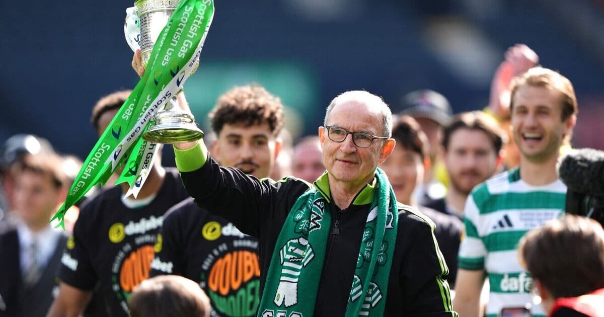 Manager holding trophy with team celebrating behind