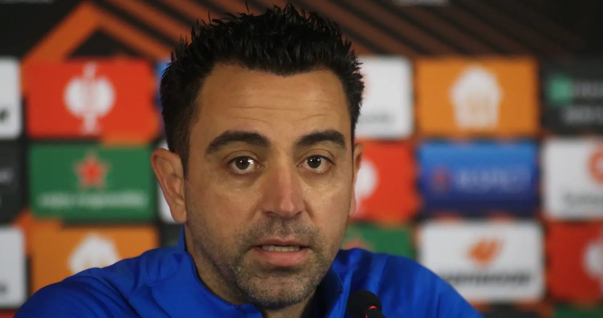 Manager speaking at press conference with sponsor banners