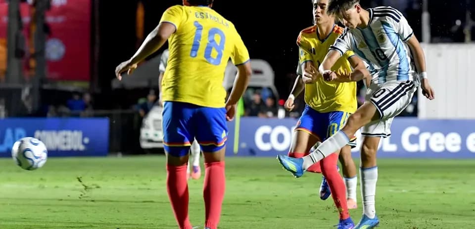 Argentinian player kicking ball past two defenders