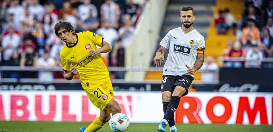 Valencia player challenges Girona player for ball
