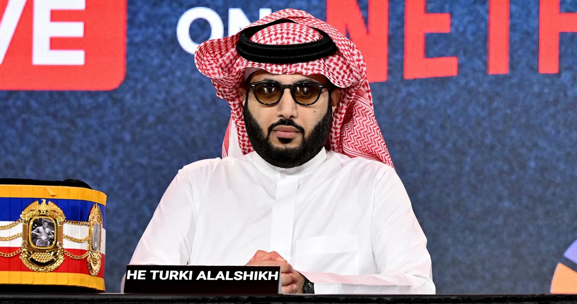 Man in traditional attire at press conference table