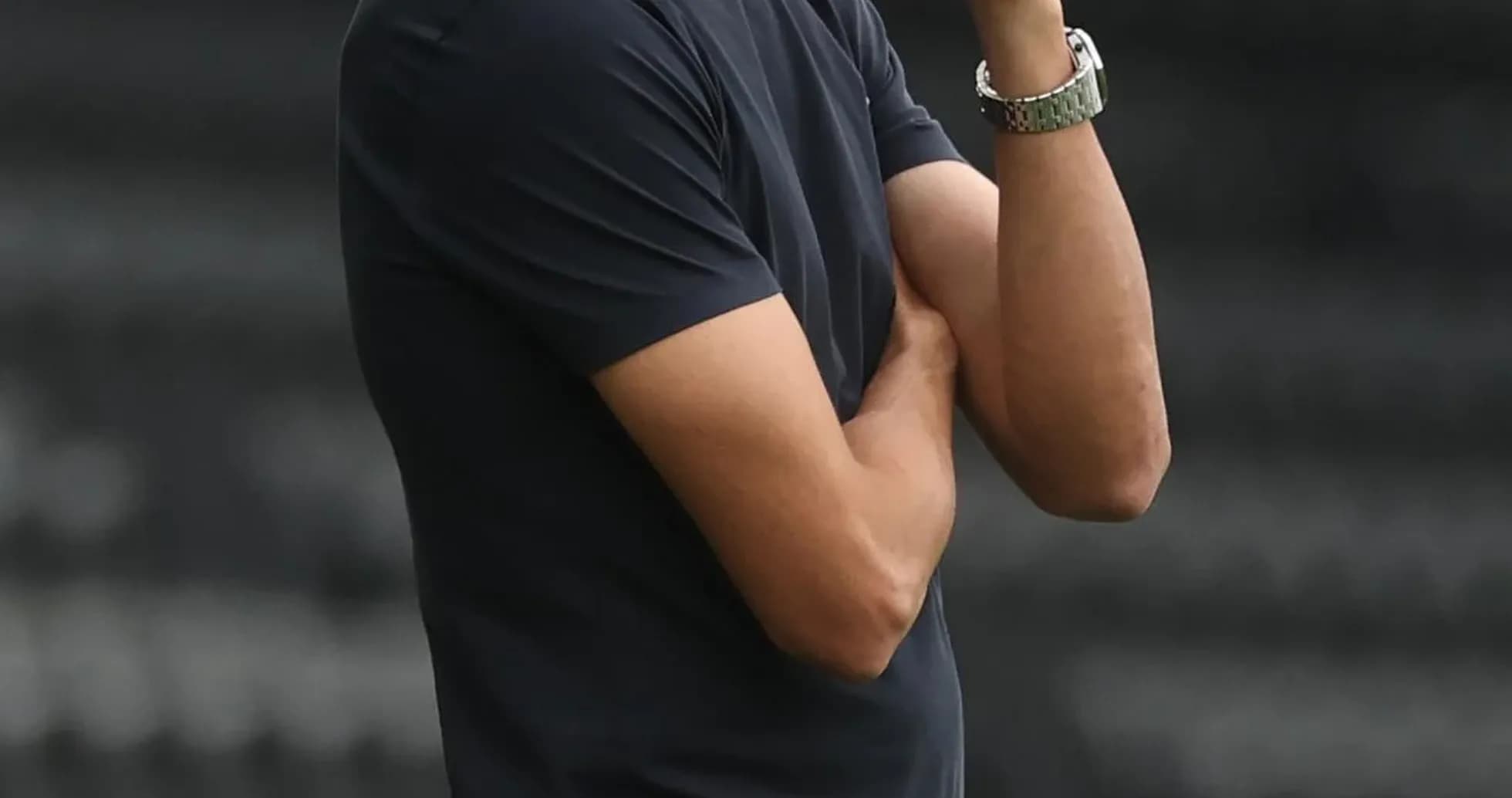 Coach observing match with arms crossed on sidelines