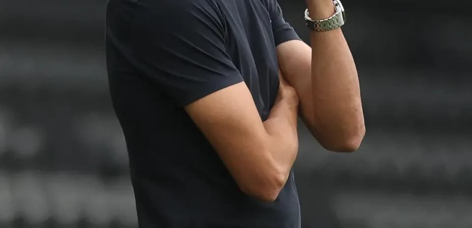 Coach observing match with arms crossed on sidelines