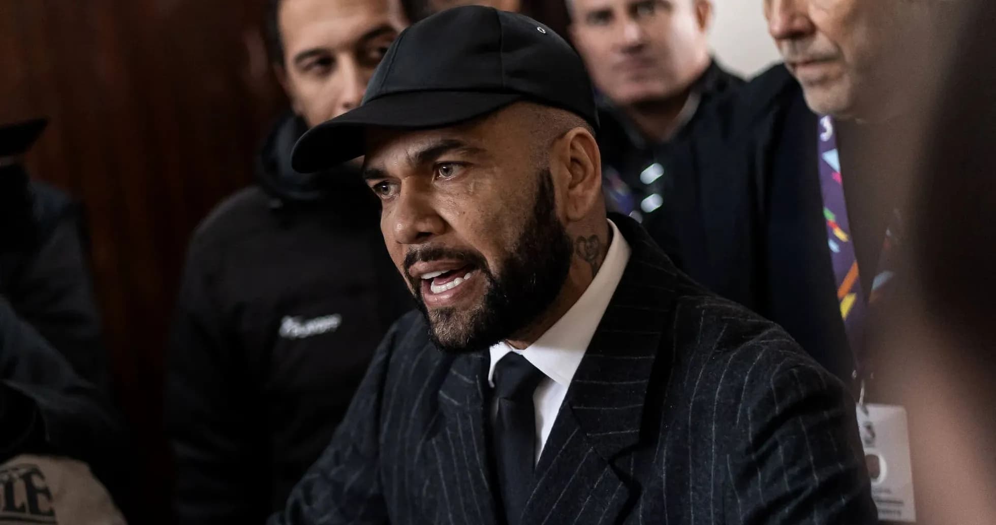 Man speaking to crowd, wearing black suit and cap