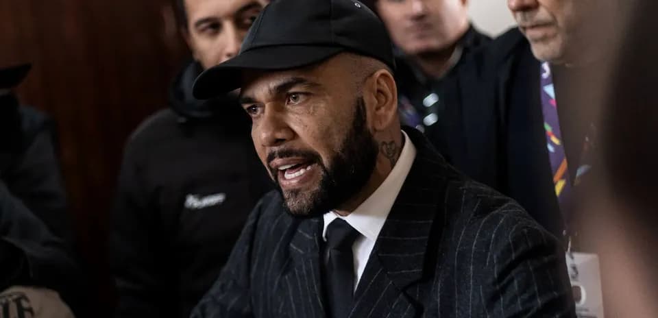 Man speaking to crowd, wearing black suit and cap