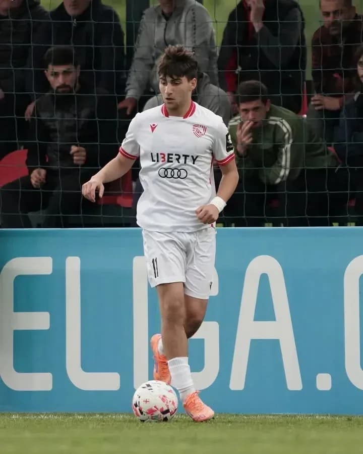 Player in white kit dribbling soccer ball on field