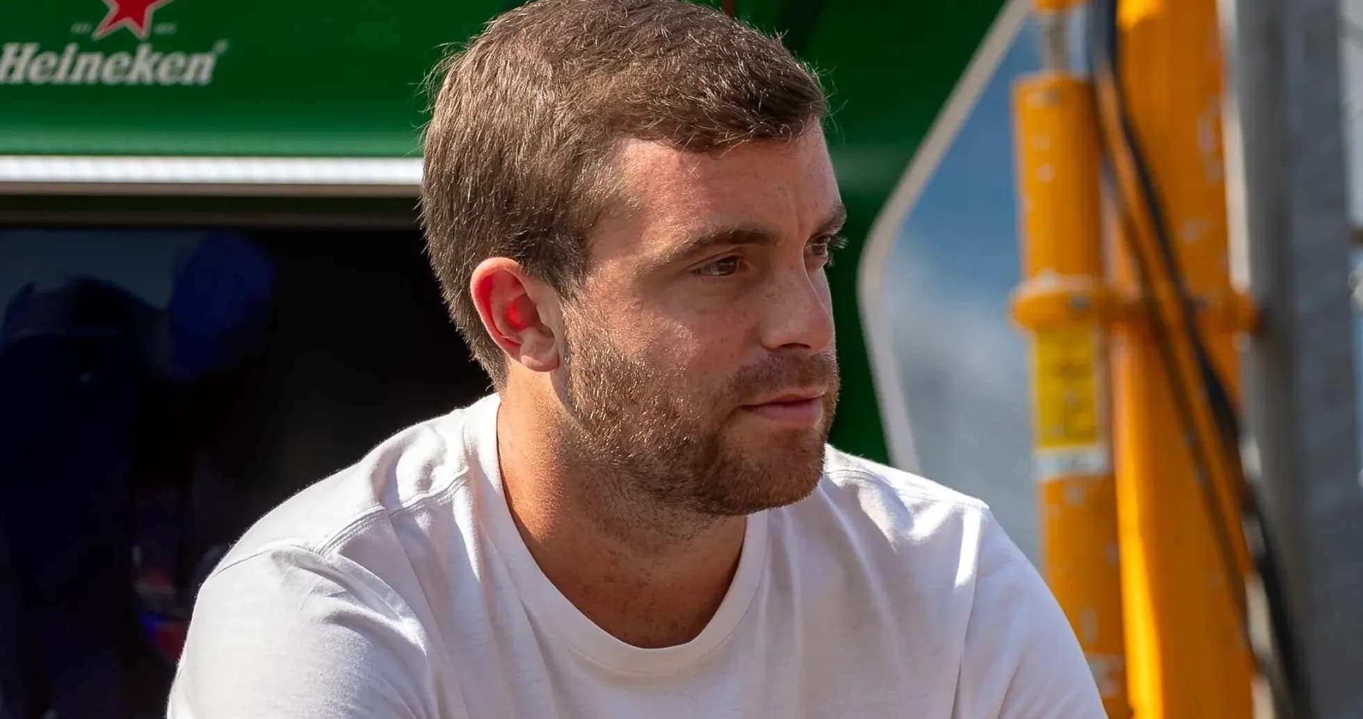 Man sitting near a green backdrop, wearing a white shirt