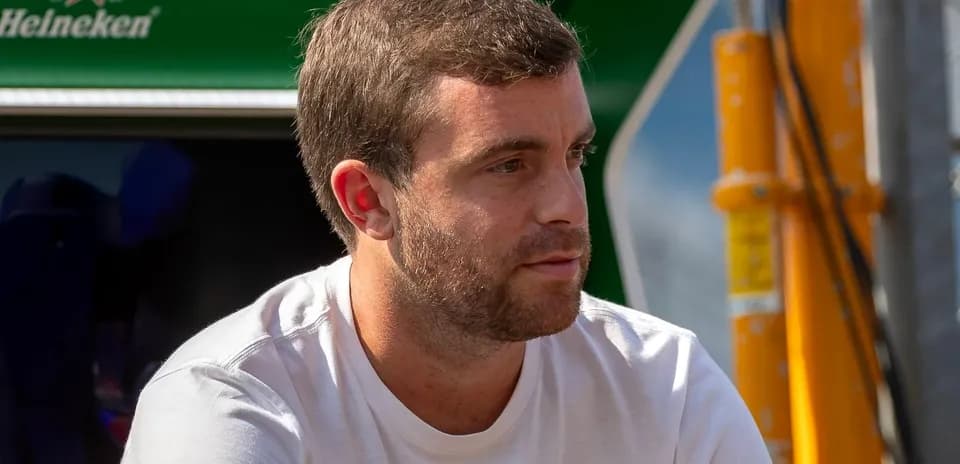 Man sitting near a green backdrop, wearing a white shirt