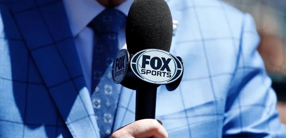 Person holding a FOX Sports microphone in blue suit