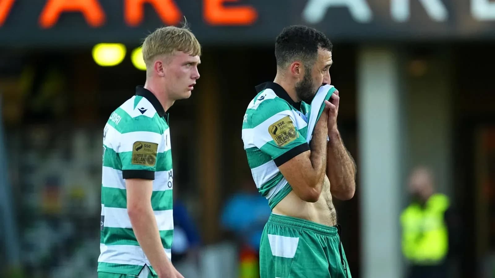 Two players in green and white jerseys walking off field
