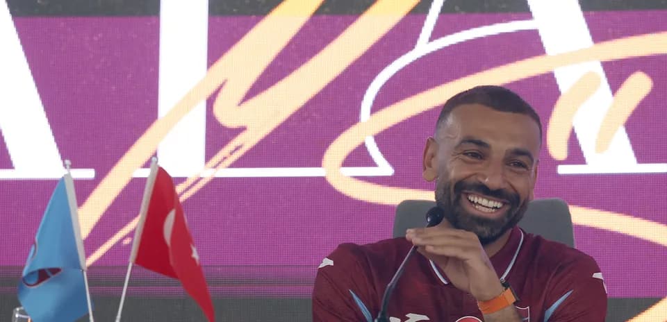 Football player speaking at press conference with flags