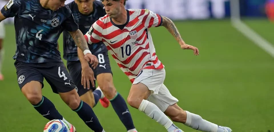 USA player dribbling past Paraguay defenders during match