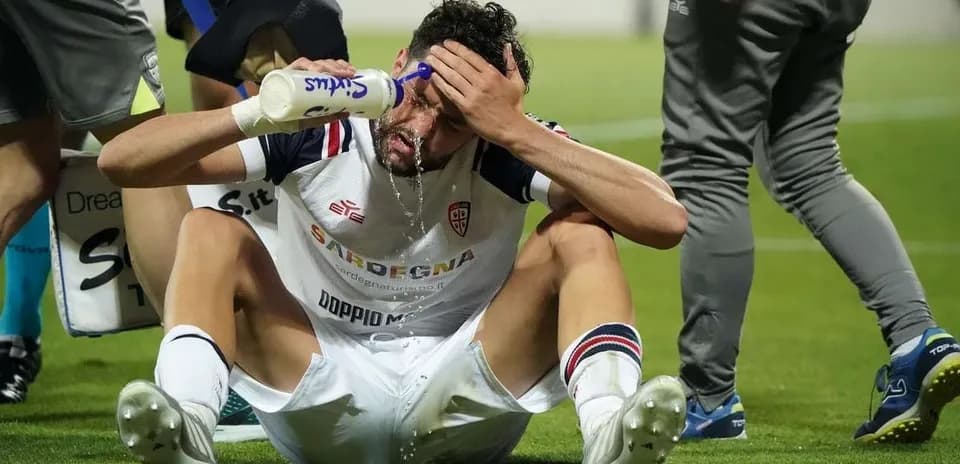Player sitting on pitch applying water to forehead