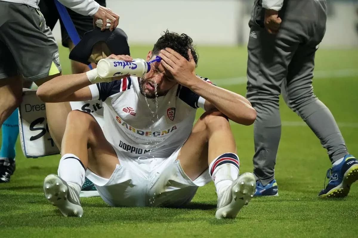 Player sitting on pitch applying water to forehead