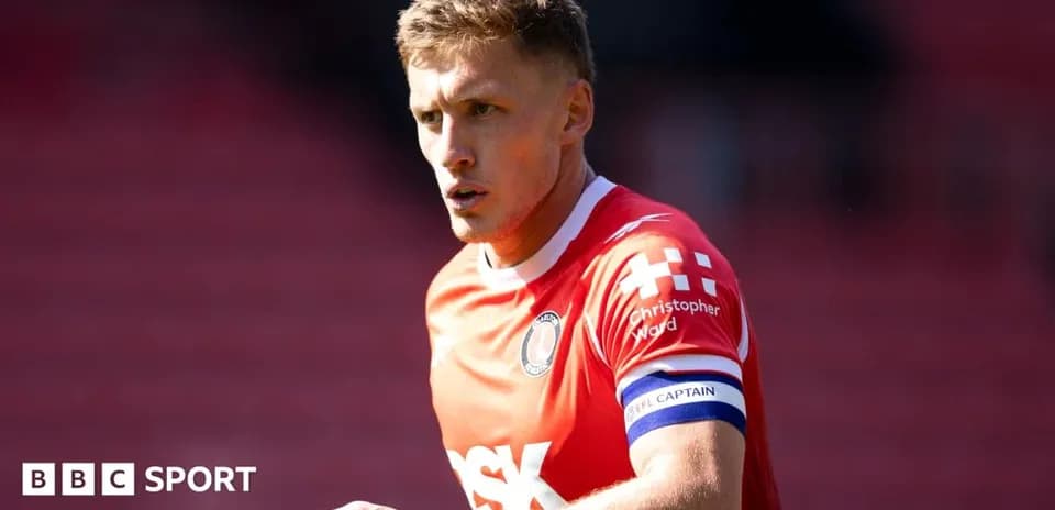 Player in red kit wearing captain's armband on field