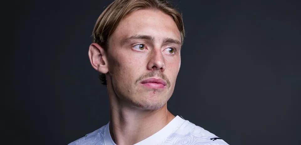 Athlete posing in white jersey against dark background