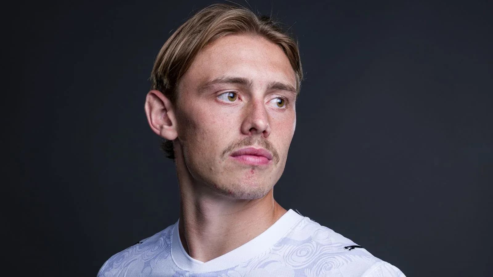 Athlete posing in white jersey against dark background