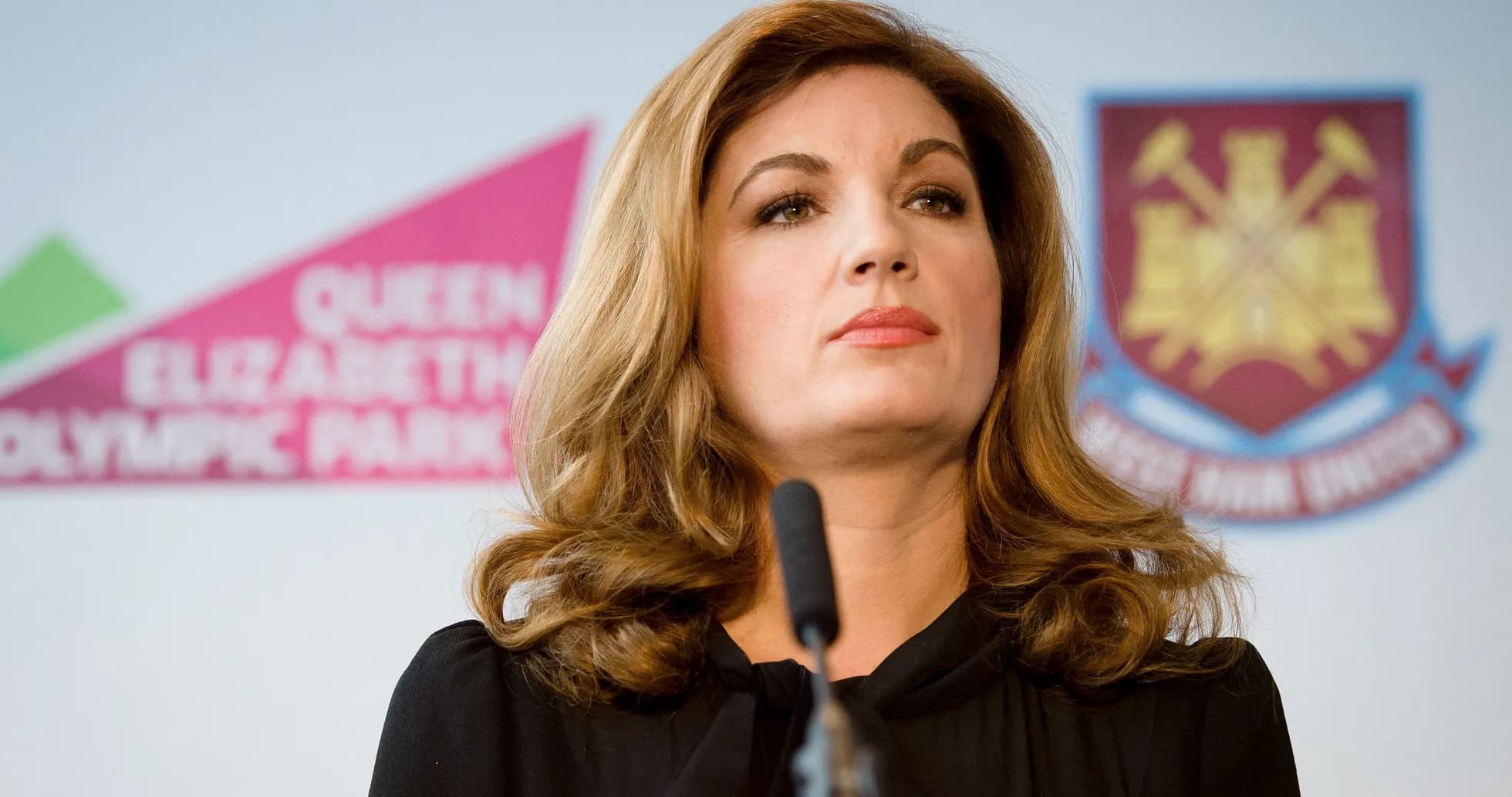 Woman speaking at press conference with logo backdrop