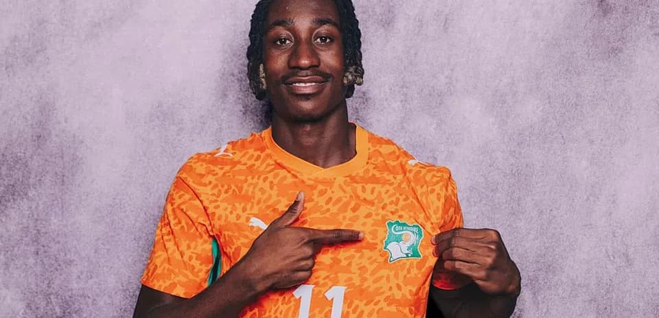 Player in orange jersey pointing at national badge