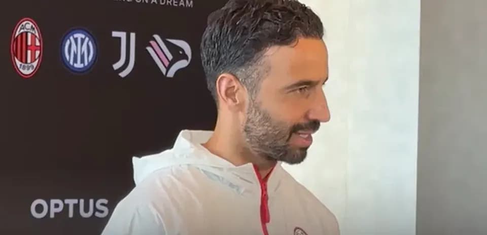 Person speaking at press conference with team logos