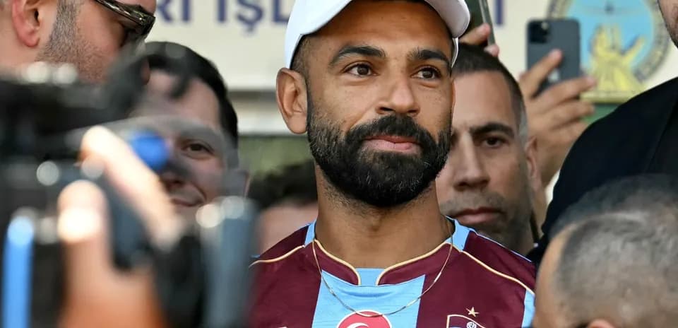 Player in Trabzonspor jersey surrounded by fans and media