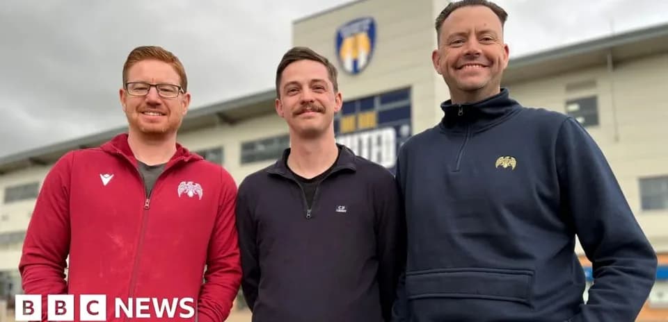 Three men posing in front of sports venue