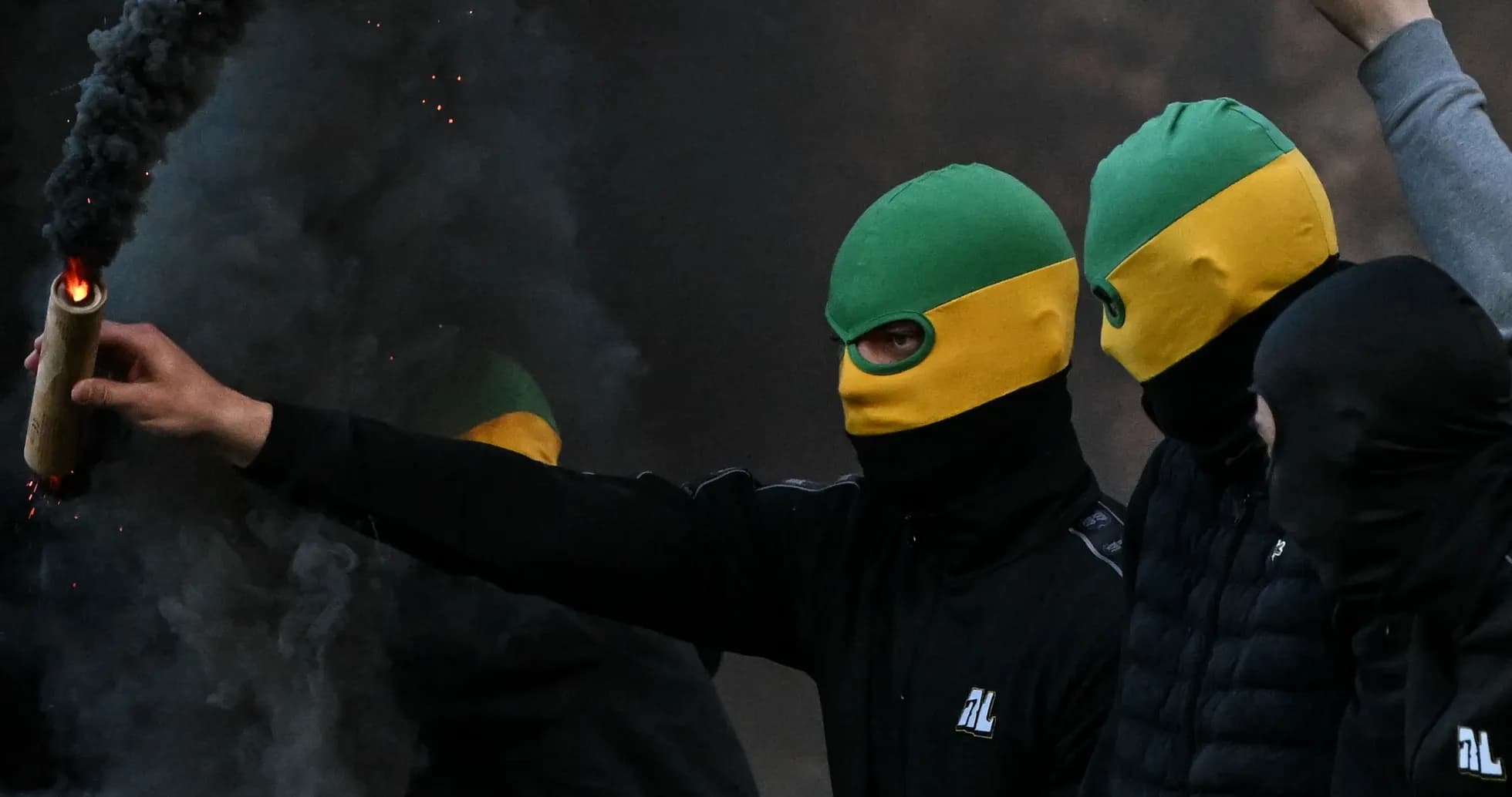 Masked individuals holding a flare amidst smoke Masked individuals holding a flare amidst smoke