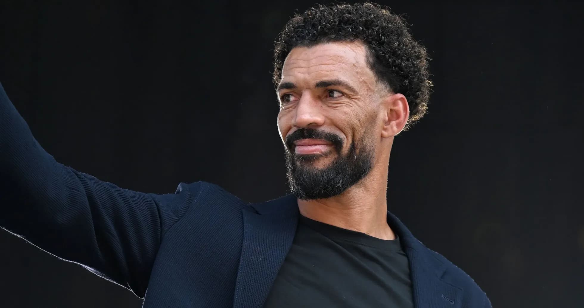 Man waving while wearing a dark blazer Man waving while wearing a dark blazer