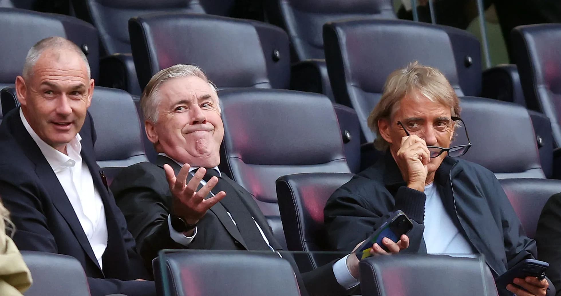 Three men seated in a stadium watching a game Three men seated in a stadium watching a game