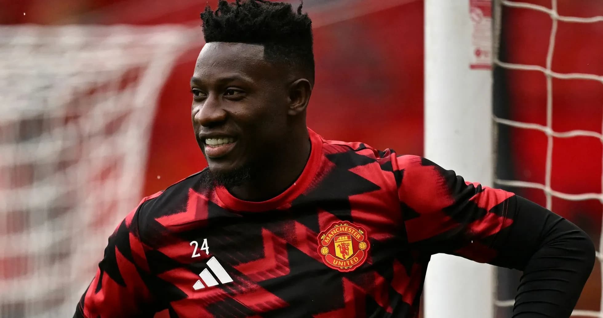 Goalkeeper in red and black kit smiling on pitch Goalkeeper in red and black kit smiling on pitch