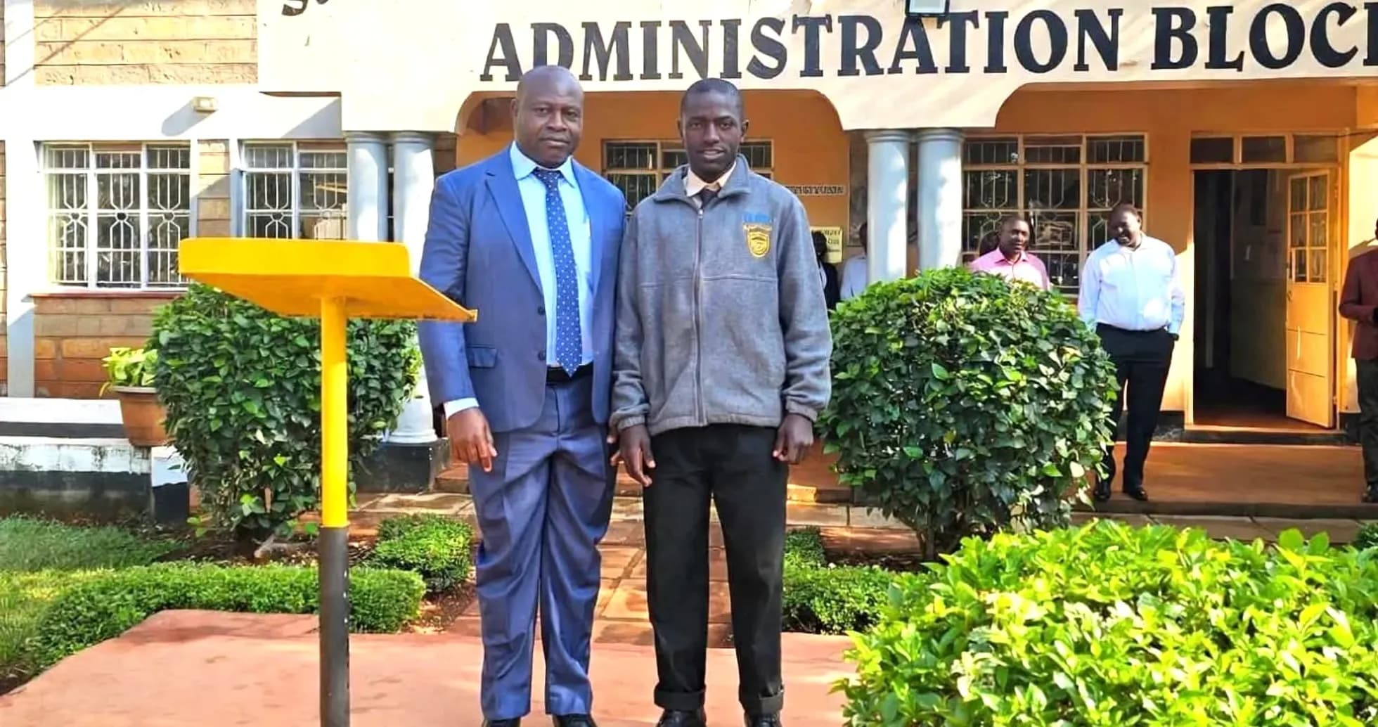 Two men posing in front of school administration block Two men posing in front of school administration block